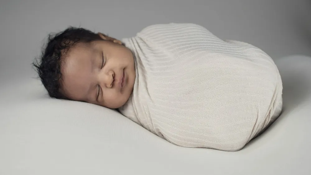 Newborn asleep in an ivory knit onesie